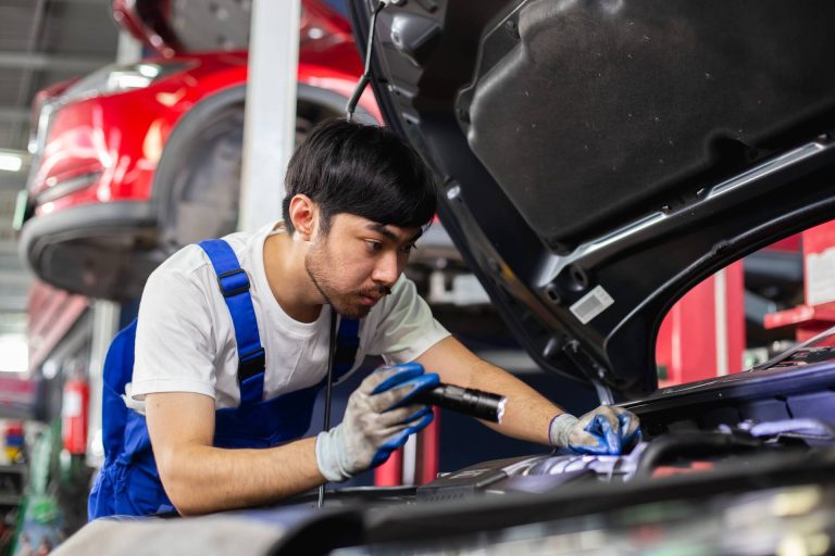 mechanic-inspecting-car-engine-with-flashlight-in-2026-01-08-06-41-56-utc-1